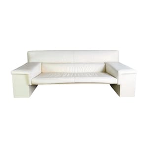 May include: A white leather sofa with a low profile and a minimalist design. The sofa features a rectangular base, armrests, and a backrest. The cushions have a slightly wrinkled texture, and the overall aesthetic is modern and clean.