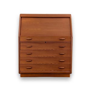 Op de afbeelding: Een middelbruin houten secretaire met een schuin naar beneden klappend voorpaneel en vier horizontale lades eronder. Elke lade is voorzien van twee ovale houten handgrepen. De houtnerf is zichtbaar over het gehele oppervlak.