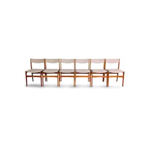 May include: Six mid-century modern dining chairs. The chairs have a light wood frame with a light-colored seat and back. The chairs are arranged in a row against a white background. The chairs are approximately 30 inches tall.