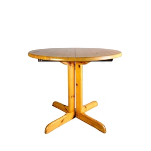 May include: A round wooden table with a natural finish and a four-legged base. The table is made of solid wood and has a simple, classic design.
