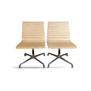 May include: Two cream-coloured office chairs with ribbed backs and chrome legs. The chairs have a low-back design and swivel bases. The legs are a star-shaped design. The chairs are set against a white background.