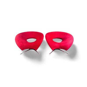 Könnte beinhalten: Zwei moderne rote Sessel mit einem einzigartigen kreisförmigen Design in der Sitzfläche. Die Stühle haben eine weiche, samtige Textur und werden von schlanken, silberfarbenen Metallbeinen getragen. Die Stühle stehen vor einem weißen Hintergrund.