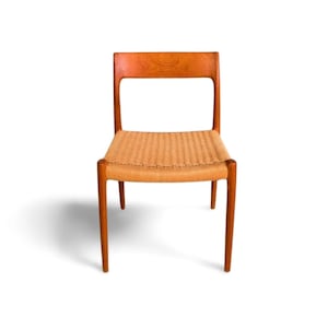 May include: A wooden chair with a woven seat. The chair has a light brown wooden frame and a rectangular backrest with a cutout. The seat is made of woven natural fibres. The chair is designed with four legs.
