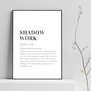 Op de afbeelding: Een ingelijste print met de woorden "SHADOW WORK" in vette, zwarte letters. Hieronder staat de definitie van schaduwwerk, die de praktijk uitlegt van het verkennen van verborgen delen van jezelf voor genezing en transformatie. De print wordt weergegeven op een wit oppervlak.