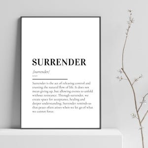 以下が含まれることがあります： 黒い文字で「SURRENDER」と書かれたフレーム入りのプリント。その下に、単語の定義が説明されています。プリントは黒いフレームに入っており、白い壁に掛けられています。