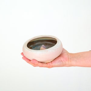 May include: A white ceramic incense burner with a brown and blue glazed interior. The burner has a small cone-shaped opening in the center.