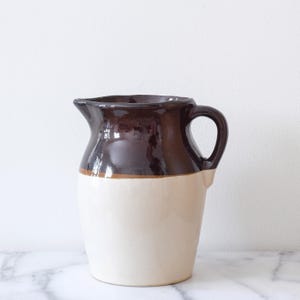 May include: A brown and white glazed ceramic pitcher with a rounded body and a handle.