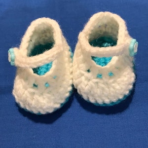 May include: A pair of white crocheted baby booties with blue trim and a blue button on each bootie.