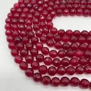 May include: A strand of deep red faceted gemstone beads. The beads are round and have a smooth, polished finish.