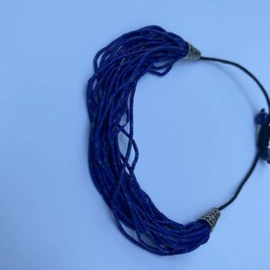 May include: A blue beaded necklace with silver metal clasps. The necklace is made of many small, round beads that are strung together on a black cord.