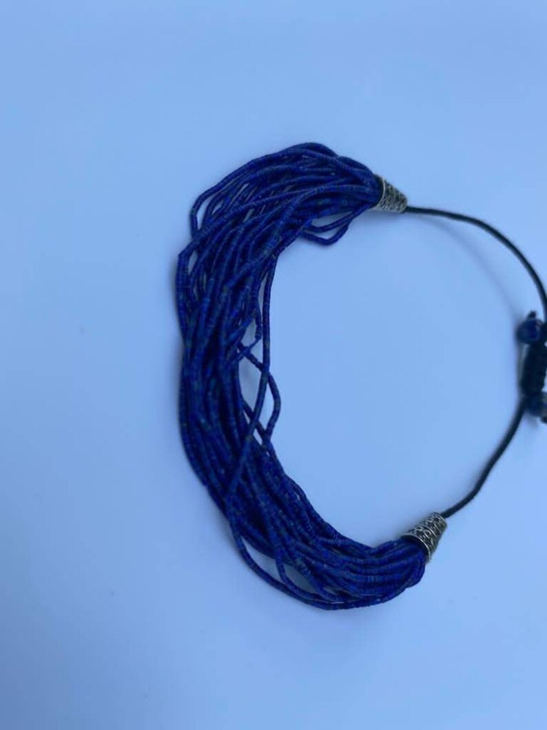 May include: A blue beaded necklace with silver metal clasps. The necklace is made of many small, round beads that are strung together on a black cord.