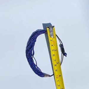 May include: A blue lapis lazuli beaded necklace with a silver clasp and a black cord with blue beads. The necklace is measured with a yellow tape measure, showing it is 10 inches long.