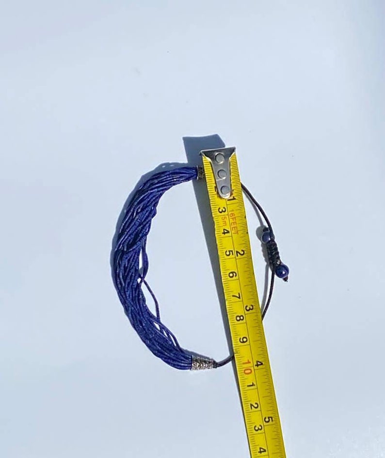 May include: A blue lapis lazuli beaded necklace with a silver clasp and a black cord with blue beads. The necklace is measured with a yellow tape measure, showing it is 10 inches long.