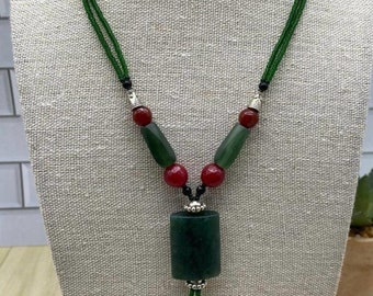 May include: A green jade necklace with red and green beads and a large green jade pendant. The necklace is on a white mannequin.