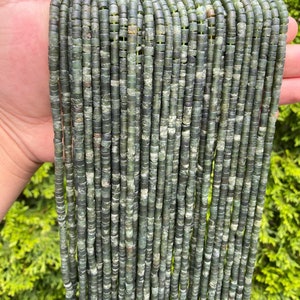 May include: A strand of green jade beads, each bead is a cylinder with a slightly irregular shape. The beads are stacked in rows, creating a visual texture.