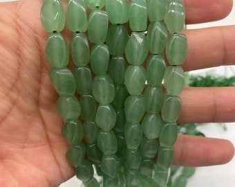 Pode incluir: Um fio de contas de jade verde claro, cada conta é facetada e tem um formato ligeiramente irregular. As contas são enfiadas em um fio fino e estão prontas para serem usadas para a fabricação de joias.