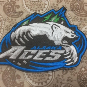 Könnte beinhalten: Gestickter Aufnäher mit einem weißen Eisbären vor einem schwarzen und blauen Hintergrund. Der Text "ALASKA ACES" ist zu sehen. Der Aufnäher hat einen blauen Rand und grüne Akzente. Zum Aufnähen auf Kleidung.