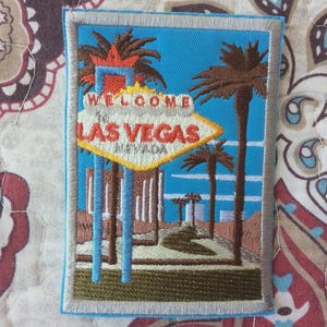Könnte beinhalten: Gestickter Aufnäher mit dem berühmten "Welcome to Las Vegas"-Schild, Palmen und blauem Himmel. Der Aufnäher hat einen hellblauen Rand und den Text "LAS VEGAS NEVADA".
