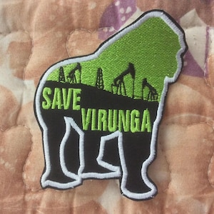 May include: Embroidered patch in the shape of a gorilla with the words "SAVE VIRUNGA" in green. The gorilla's body is black with white trim. The green interior features oil derricks, symbolizing environmental conservation.