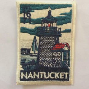 Puede incluir: Parche bordado con un faro con tejado rojo y la palabra "NANTUCKET" en blanco. El parche incluye un velero y el número "16" con un ancla. El diseño es en tonos azules, verdes y rojos.
