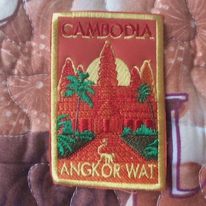 Puede incluir: Parche bordado con el templo de Angkor Wat en Camboya. El parche es rectangular con fondo rojo y borde amarillo. Los textos "CAMBODIA" y "ANGKOR WAT" están bordados en dorado.