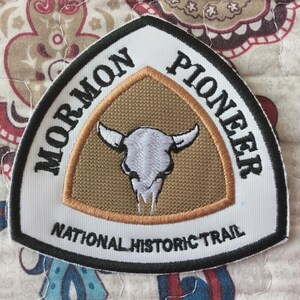Könnte beinhalten: Gestickter Aufnäher mit den Worten "MORMON PIONEER NATIONAL HISTORIC TRAIL". Der Aufnäher hat einen weißen Rand, einen beigefarbenen Hintergrund und ein stilisiertes Bild eines Bullenschädels.