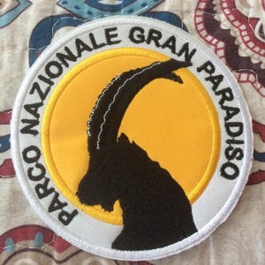 Può includere: Toppa ricamata rotonda con una silhouette nera di stambecco su sfondo giallo. La toppa è bordata di bianco e presenta la scritta "PARCO NAZIONALE GRAN PARADISO". Un souvenir.