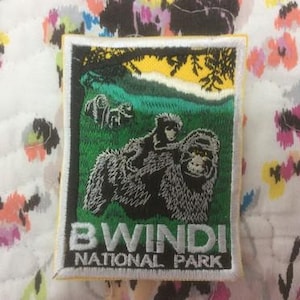 Op de afbeelding: Geborduurde patch met een gorilla met een babygorilla op zijn rug, tegen een groene en gele achtergrond. De patch heeft de tekst "BWINDI NATIONAL PARK" in witte letters op een zwarte achtergrond.