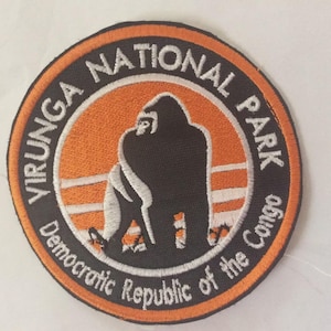 May include: Embroidered patch featuring the words "VIRUNGA NATIONAL PARK" and "Democratic Republic of the Congo" in a circular design. The patch has an orange and black color scheme with a gorilla silhouette in the center.