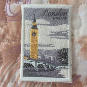 Peut inclure: Écusson brodé représentant Londres, Angleterre. Le design comprend Big Ben en jaune et gris, un pont et une grande roue. Le mot "London" est écrit en haut, avec "England" en dessous.