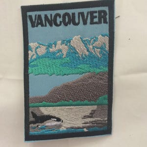 May include: Embroidered patch featuring the word "VANCOUVER" above a scenic landscape. The design includes mountains, a lake, and an orca whale. The patch has a black border and a light blue background.