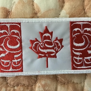 May include: A rectangular embroidered patch featuring a stylized Canadian flag design. The patch has a white center with a red maple leaf and two red side panels, each decorated with intricate white embroidered patterns and a white border.