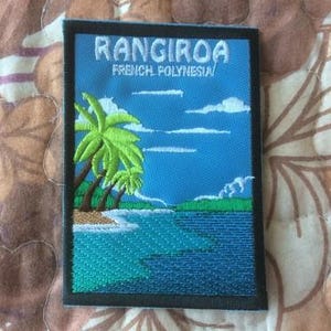 Könnte beinhalten: Gestickter Aufnäher mit einer tropischen Szene mit Palmen, Ozean und dem Text "RANGIROA FRENCH POLYNESIA" in Weiß. Der Aufnäher hat einen schwarzen Rand und einen blauen Hintergrund, der an Reisen und Abenteuer erinnert.