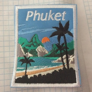 May include: Embroidered patch featuring a tropical beach scene with the word "Phuket" in white. The design includes palm trees, mountains, a sunset, and ocean waves in shades of blue, green, and orange.