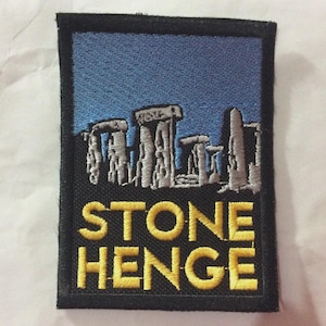 May include: Embroidered patch featuring Stonehenge under a blue sky. The patch has a black border and the words "STONE HENGE" in yellow block letters. The design depicts the iconic prehistoric monument.