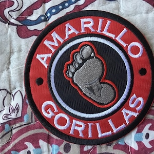 Op de afbeelding: Een ronde geborduurde patch met een zwart midden en een grijze voetafdruk-afbeelding. De patch heeft een rode rand met de witte tekst AMARILLO GORILLAS in een cirkelvormig patroon geborduurd. Het ontwerp is afgewerkt met een zwarte buitenrand.