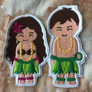 Könnte beinhalten: Zwei bestickte Stoffaufnäher mit Zeichentrickfiguren in traditioneller Hula-Kleidung. Eine Figur hat langes braunes Haar mit einer rosa Blume, ein schwarzes Oberteil, einen grünen Blätterrock und eine gelbe Kette. Die andere Figur hat kurzes braunes Haar.