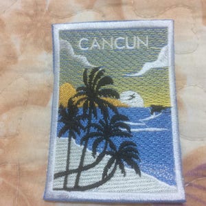 May include: Embroidered patch featuring a tropical beach scene with palm trees, ocean, and the word "CANCUN" in white. The patch has a white border and is set against a blue sky and ocean. The design includes yellow and blue hues.