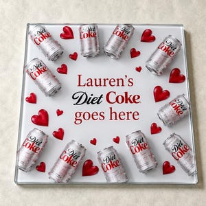 May include: A square white tray featuring the text Lauren's Diet Coke goes here in red and black lettering. The tray is decorated with twelve silver Diet Coke soda cans and several small red heart shapes arranged in a circular pattern.