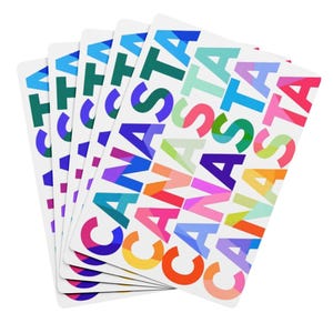 May include: A stack of white cards with the word "CANASTA" printed repeatedly in various colors. The colors include green, blue, purple, orange, and pink. The cards are fanned out, showing the design.
