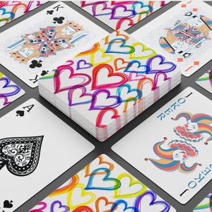 May include: A deck of playing cards with a colorful heart design on the card backs. The deck is surrounded by individual playing cards, including a Joker, Ace of Spades, and King of Clubs. The hearts are in shades of red, pink, blue, yellow, and purple.