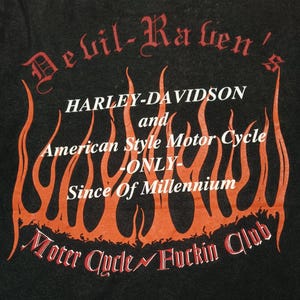May include: A black t-shirt featuring a graphic print with orange flames and white text that reads Devil-Raven's, HARLEY-DAVIDSON and American Style Motor Cycle -ONLY- Since Of Millennium, and Moter Cycle Fuckin Club at the bottom.