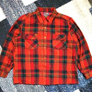 Puede incluir: Una camisa de manga larga con botones y un vibrante patrón de cuadros en rojo, verde y amarillo. La camisa incluye un cuello puntiagudo, cierre frontal de botones y dos bolsillos en el pecho con solapas abotonadas. La tela es texturizada.