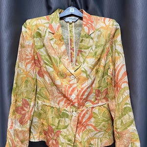 May include: A floral blazer with a tropical print in shades of orange, green, and yellow. The blazer has a two-button closure, notched lapels, and two front pockets. The brand name "Mazako" is visible on the label.