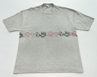 May include: A gray short-sleeved t-shirt with a crew neck. The shirt features a horizontal design of stylized dragons in black and pink across the chest. The shirt is made of a soft, comfortable material.