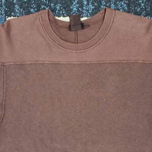 Pode incluir: Uma camisola de cor malva com gola redonda e mangas compridas. A sec&ccedil;&atilde;o superior da camisa tem uma textura canelada, enquanto a sec&ccedil;&atilde;o inferior &eacute; lisa. A camisa tem uma etiqueta na parte de tr&aacute;s do pesco&ccedil;o.