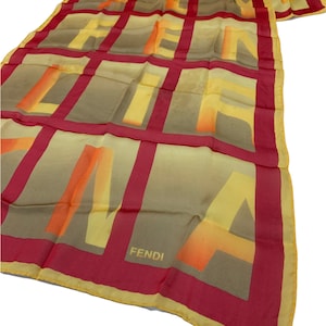 May include: A yellow and orange silk scarf with a red border and the word "FENDI" printed in the bottom right corner. The scarf features a repeating pattern of the letters "FENDI" in a grid.