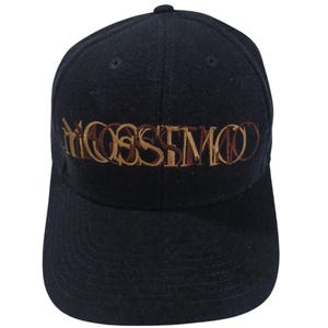 May include: A black baseball cap with the embroidered word "MOSSIMO" in brown and tan. The cap has a curved brim and a rounded top. The hat is made of a textured fabric.