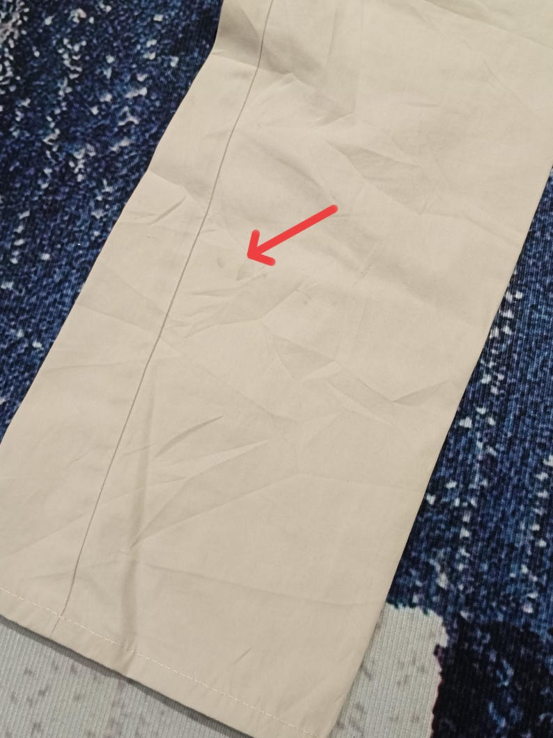 May include: Close-up of beige trousers with a central seam. The fabric is a light, neutral colour, possibly cotton or similar. The trousers are folded, and the fabric has a slightly wrinkled texture.