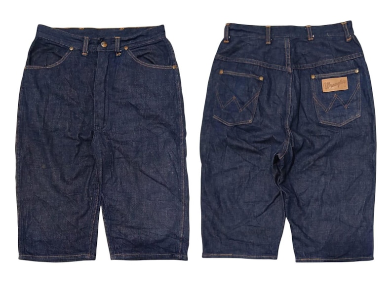 May include: Dark wash denim shorts with a classic five-pocket design. The shorts feature a button and zipper closure, belt loops, and the Wrangler brand patch on the back. The shorts are shown from the front and back.